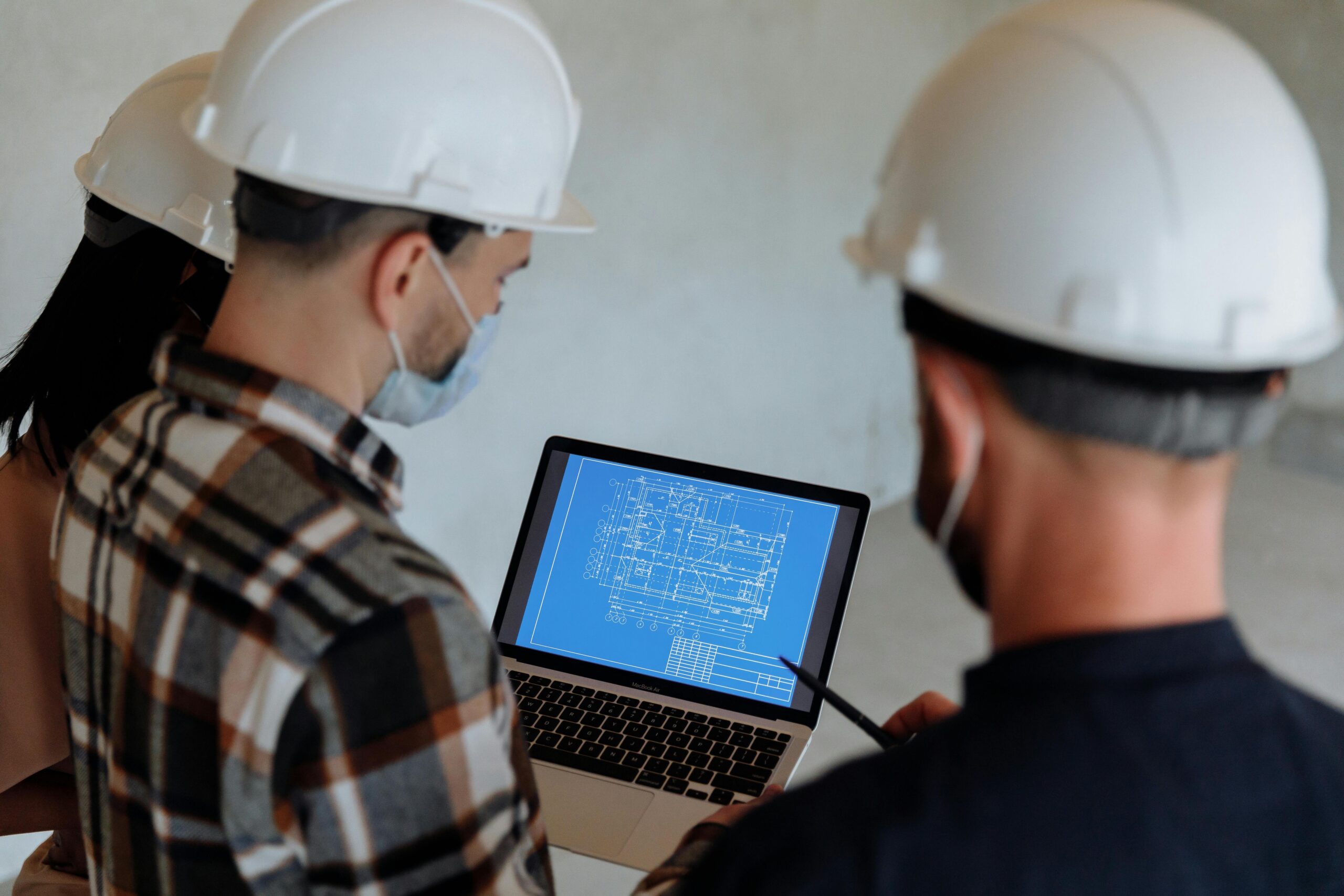 Two people in hard hats reviewing a blueprint on a laptop during planning preparation.